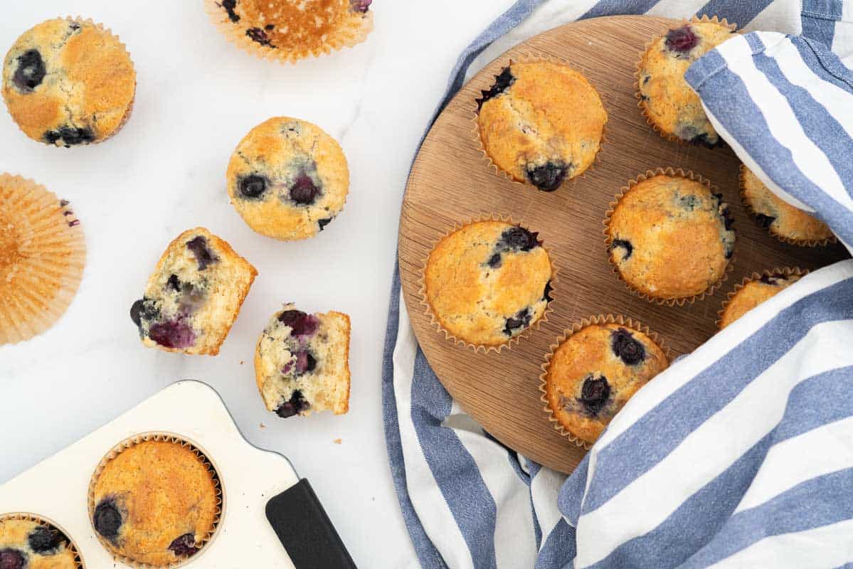 A collection of muffins on a bench top, one broken open to show it's light fluffy texture.