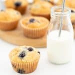 A blueberry muffin sitting next to a glass of milk with a straw.