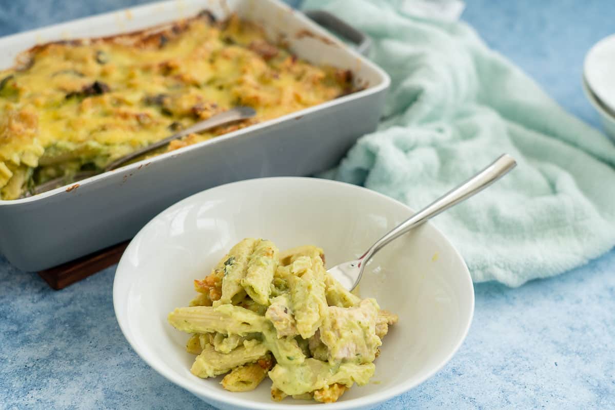 Chicken pasta bake with spinach visible in a white bowl with fork.