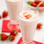 Two strawberry milkshakes in tall glasses topped with strawberry slice with red napkins.