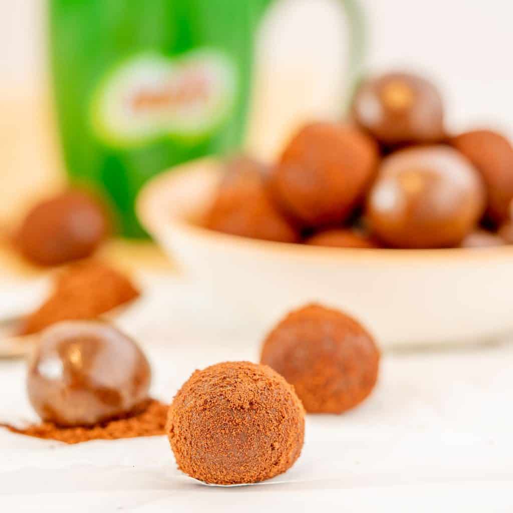 A chocolate ball rolled in milo powder sitting in front of a bowl of milo balls.