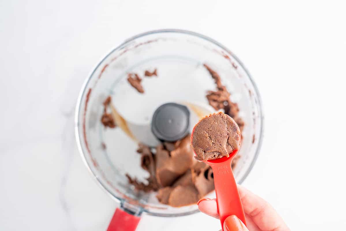 A woman's hand holding a tablespoon of milo ball mix.