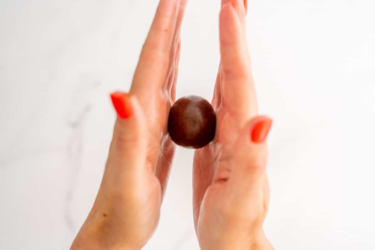 A chocolate bliss ball being rolled smooth between two hands.