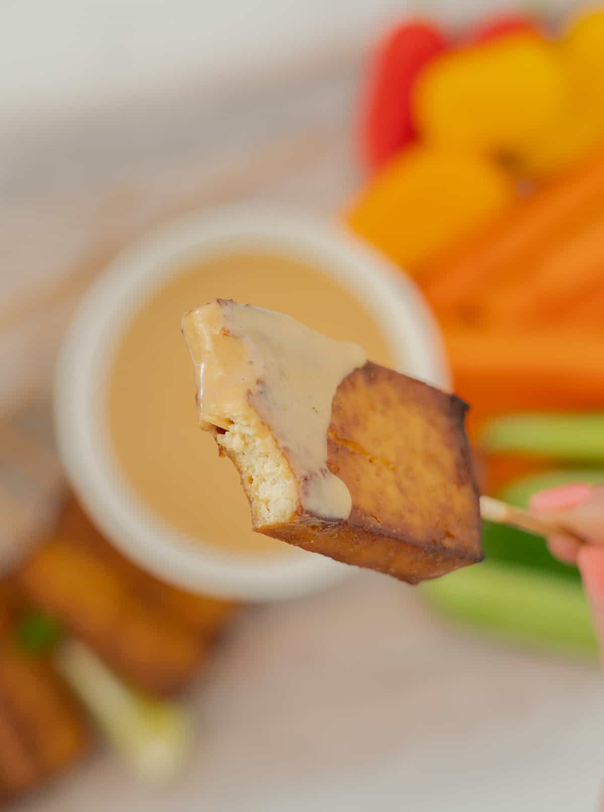A hand holding a piece of baked tofu on a skewer, a mouthful has been eaten, revealing the creamy white centre of the tofu.