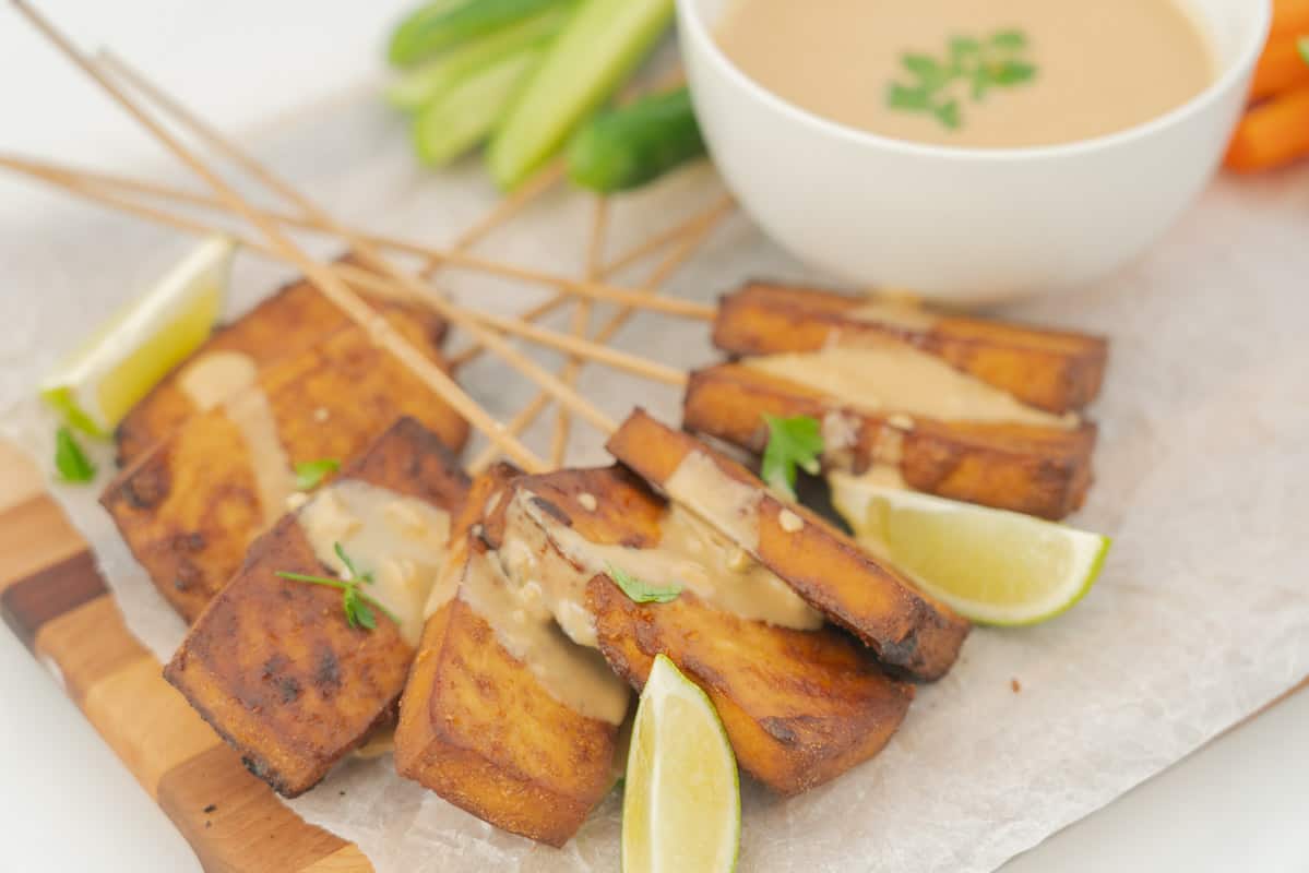 Golden brown satay tofu, drizzled with satay sauce on a serving plate.