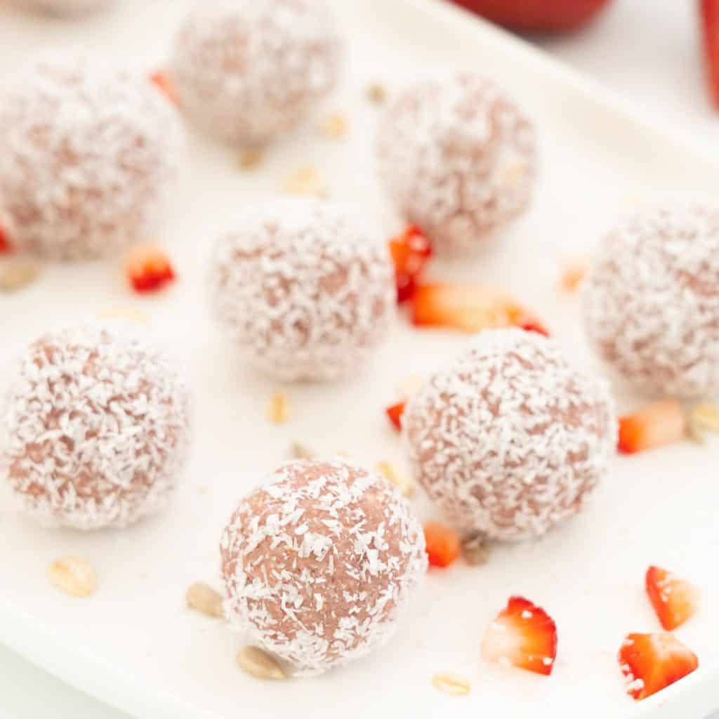 strawberry balls rolled in desiccated coconut sitting evenly spaced on a white platter.