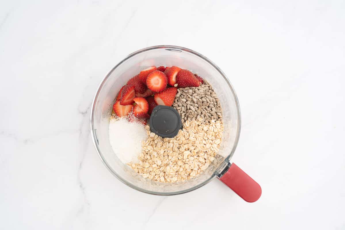 Strawberries, oats, sunflower seeds, coconut in a food processor ready to be blitzed.
