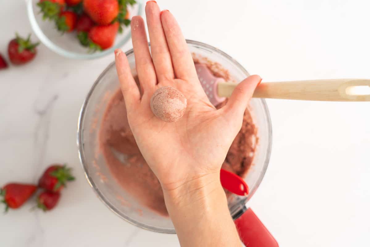 A woman's hand holding a smooth pink strawberry bliss ball.