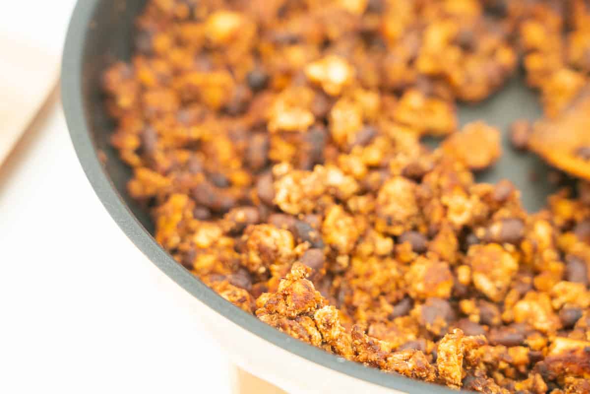close up of cooked mexican flavoured tofu crumbles in a skillet, black beans also visible.