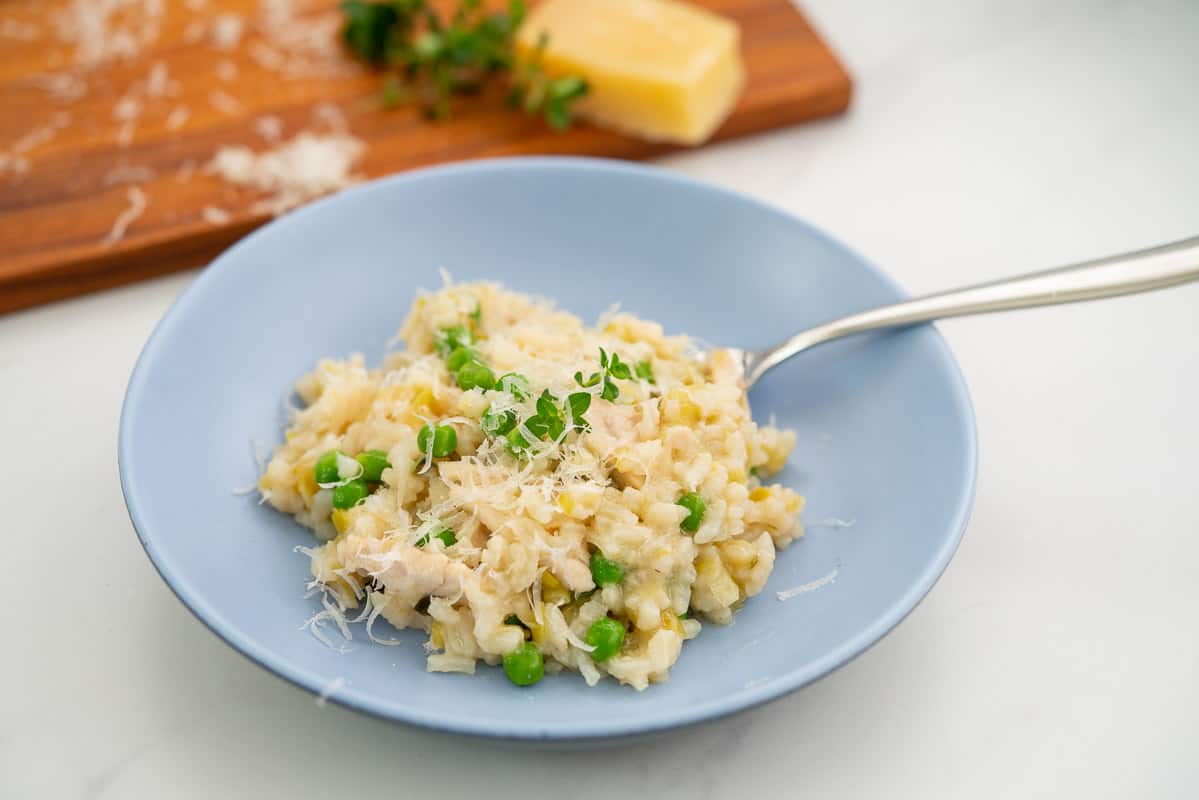 A blue bowl filled with risott, leeks, chicken and peas visible