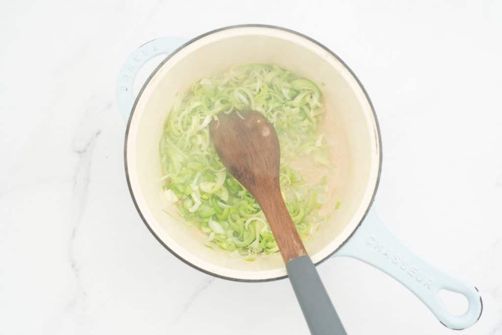 Leeks being sautéd in a large ceramic sauce pan.