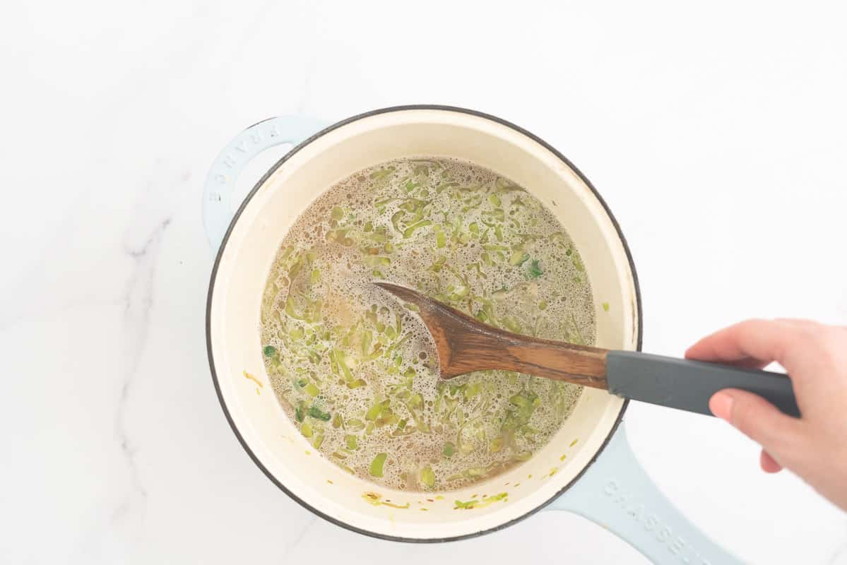A large ceramic pot filled with stock, sliced leek and arborio rice.
