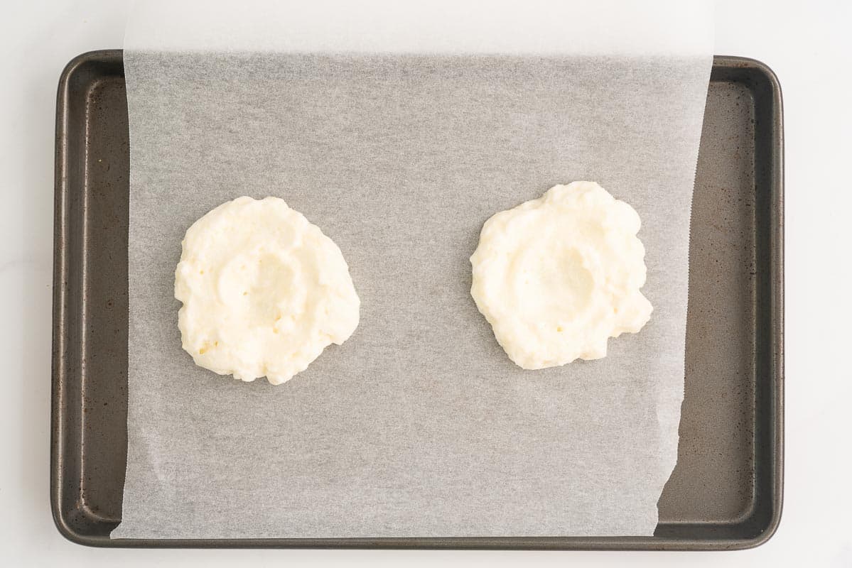 Beaten egg whites shaped like 2 clouds with a small indentation in the centre of each one.