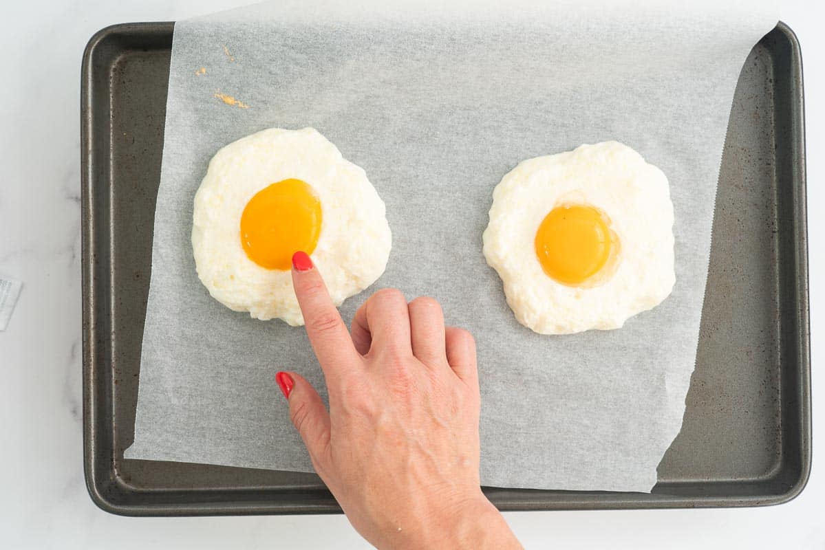 Woman's hand pointing to an egg yolk in the centre of a baked cloud shaped meringue.