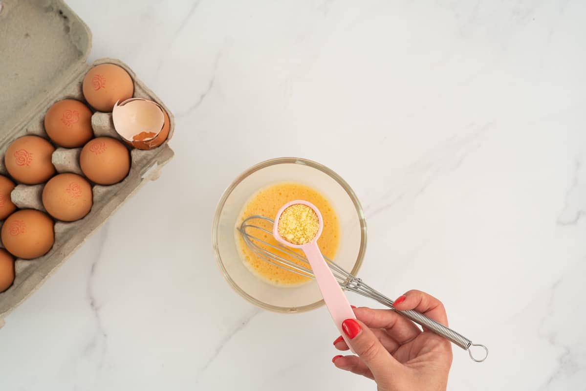 measuring spoon of parmesan being added to a beaten egg.