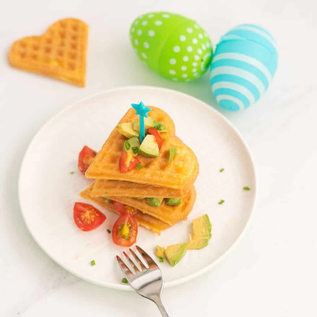 heart shapped waffles stacked up on a white plate with easter eggs in the background.