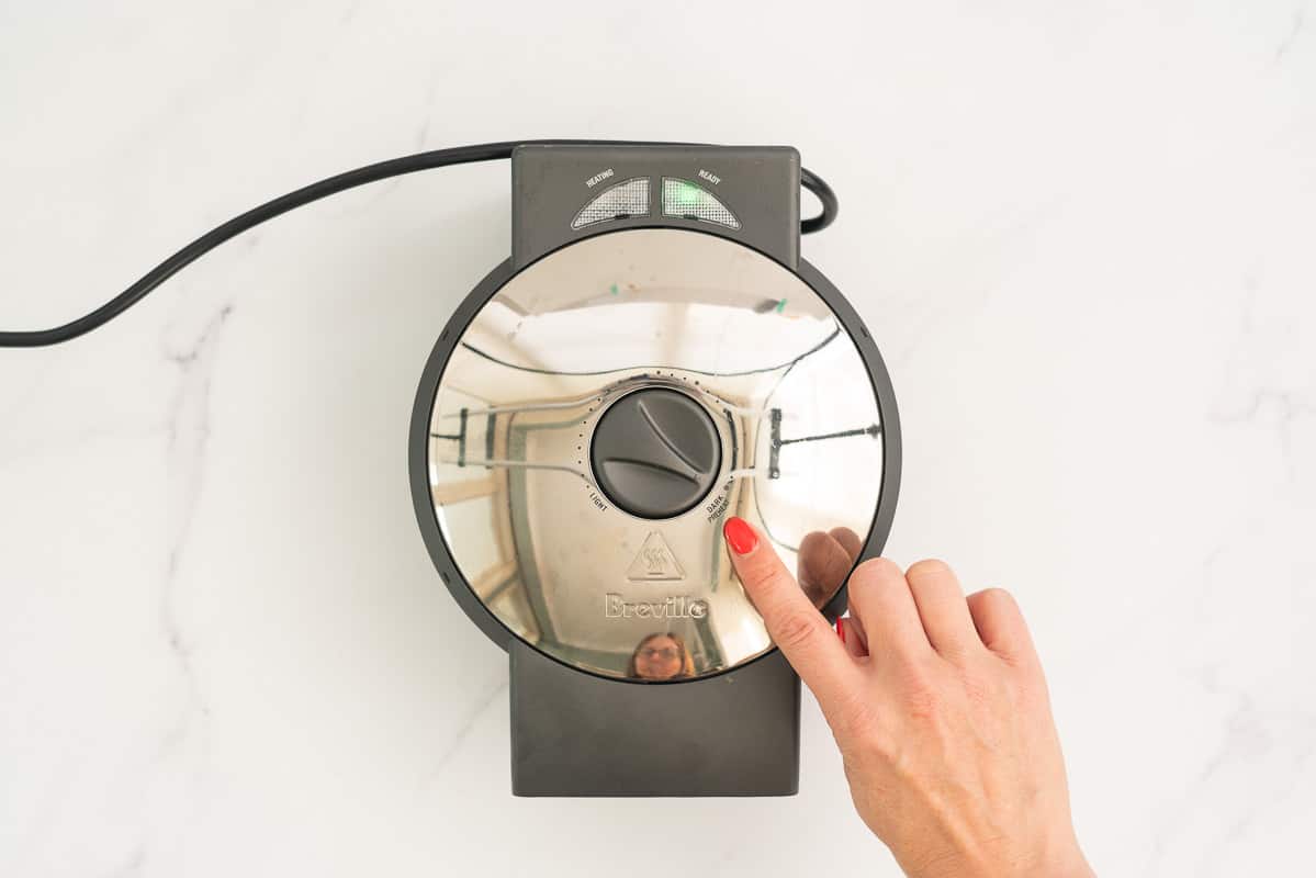 Women's hand pointing to the high setting on a waffle iron