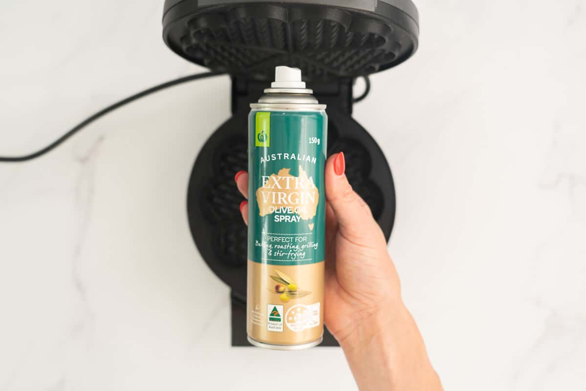 A bottle of oil spray held above a waffle maker.