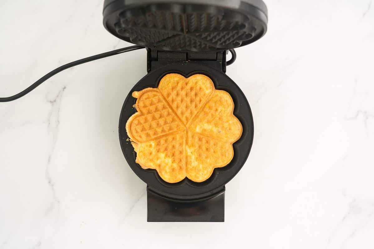A golden cooked egg waffle sitting in an open waffle maker.