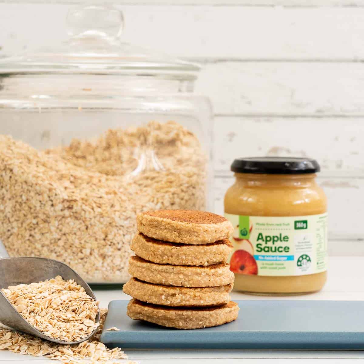 A stack of baby pancakes sitting in front of a jar of unsweetened apple sauce.