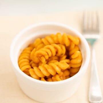 Sauce covered pasta spirals in a small white ceramic bowl.