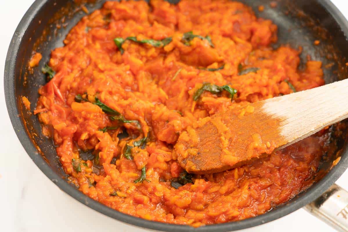 Cooked baby pasta sauce with wilted spinach leaves visible in a fry pan with a wooden spoon.