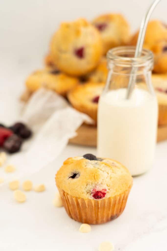 A berry muffin sitting next to a glass of milk with a straw.