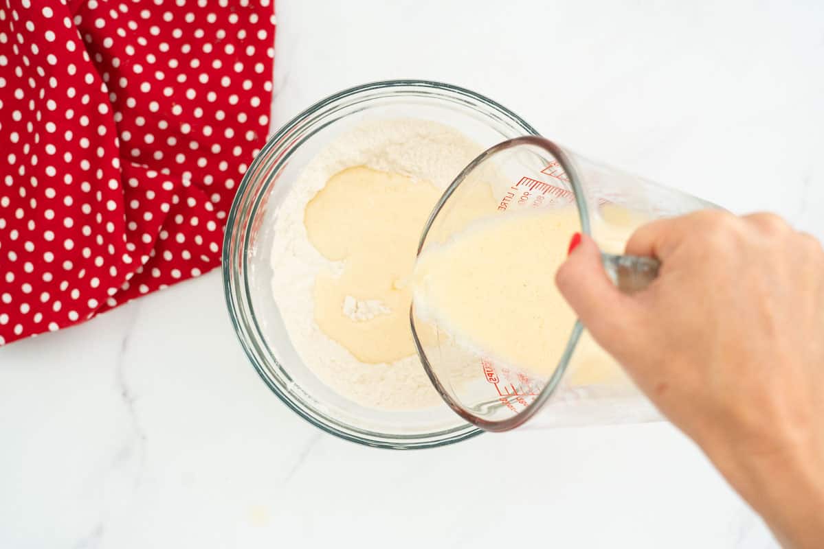Jug of wet ingredients being poured into a bowl of dry ingredients.