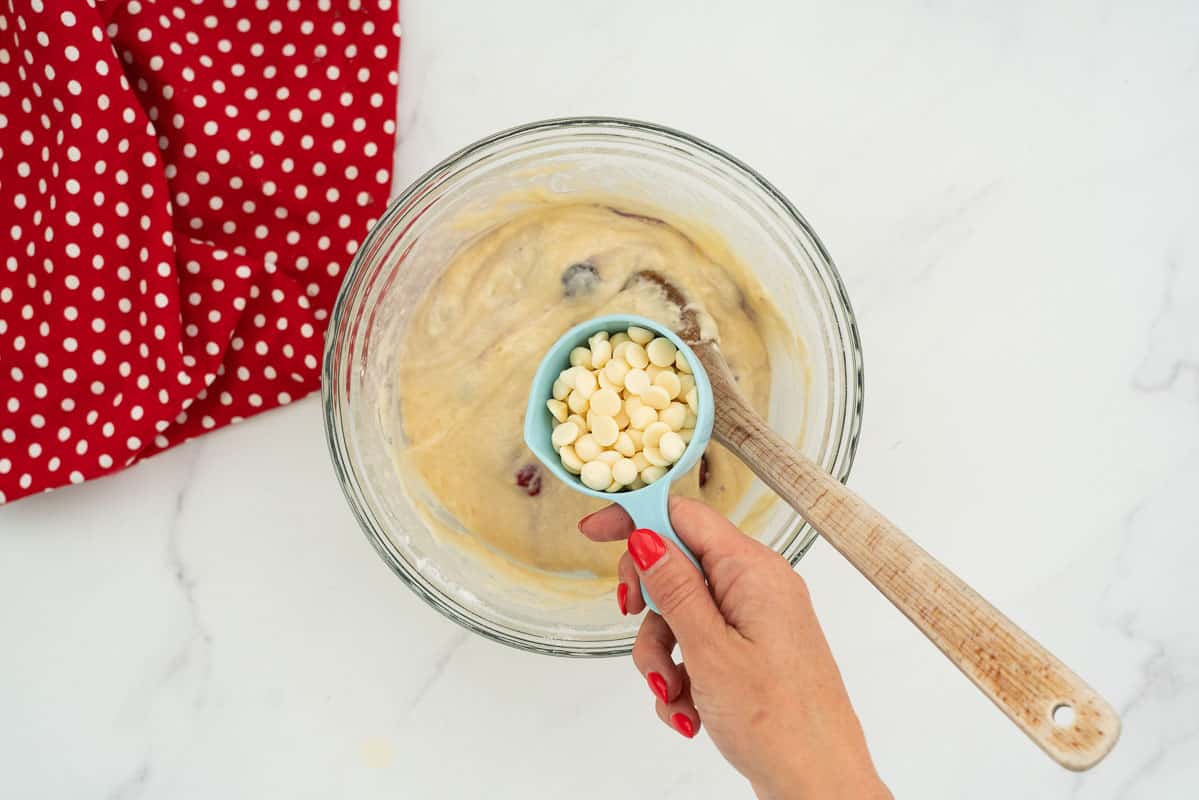 White chocolate chips being added to a bowl of berry muffin batter