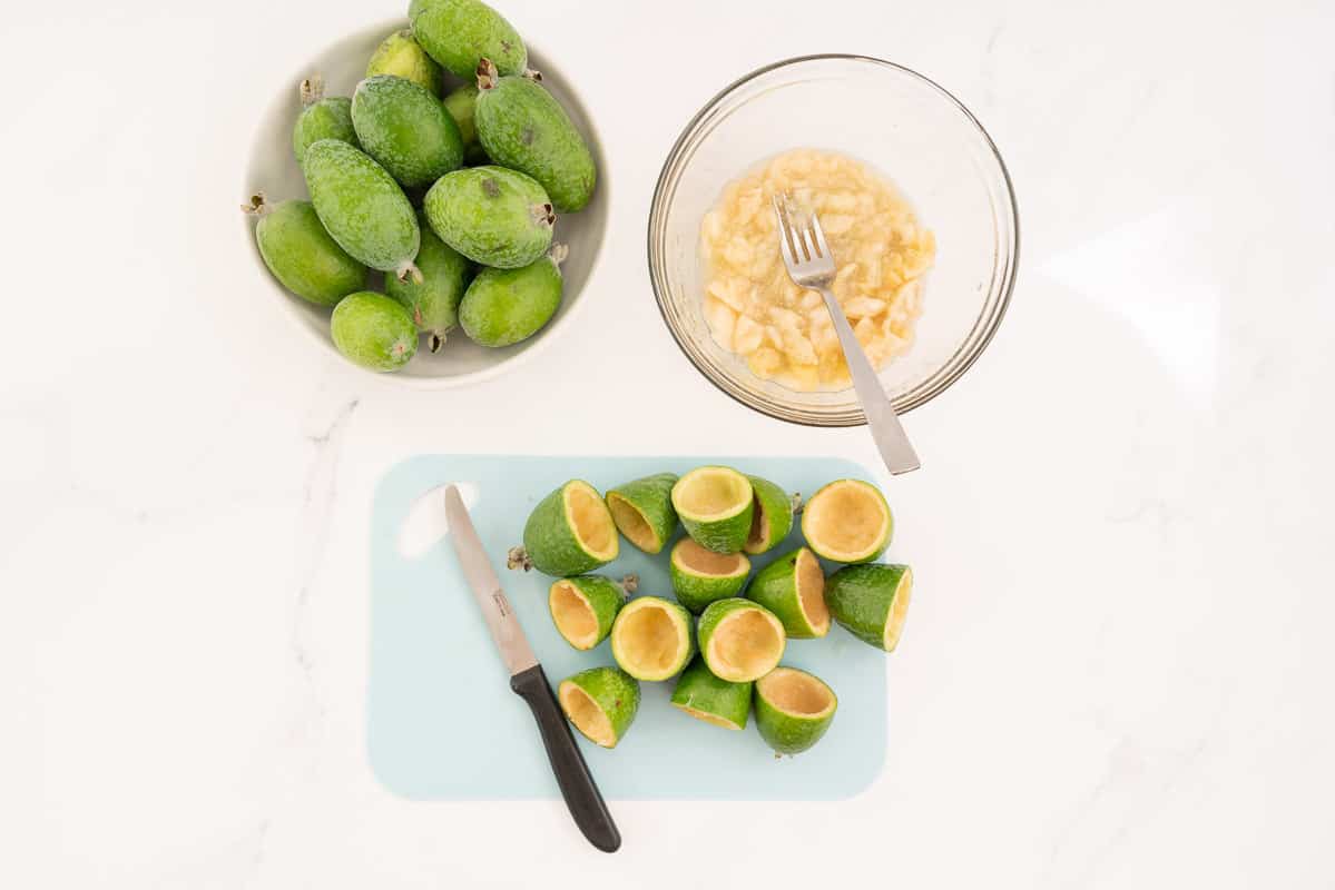Feijoa skins on a blue chopping bowl, feijoa flesh in a glass bowl with a fork.