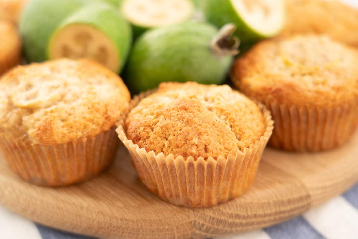 Golden muffins sitting on a wooden board with fresh feijoas.