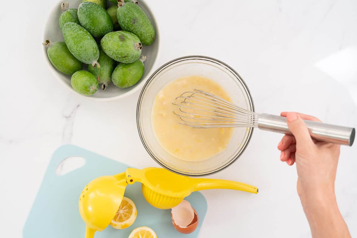 Feijoa flesh, lemon rind, egg, oil and vanilla being well combined in a glass bowl.