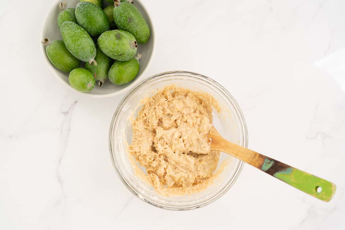 feijoa muffin batter in a glass bowl with a wooden spoon.