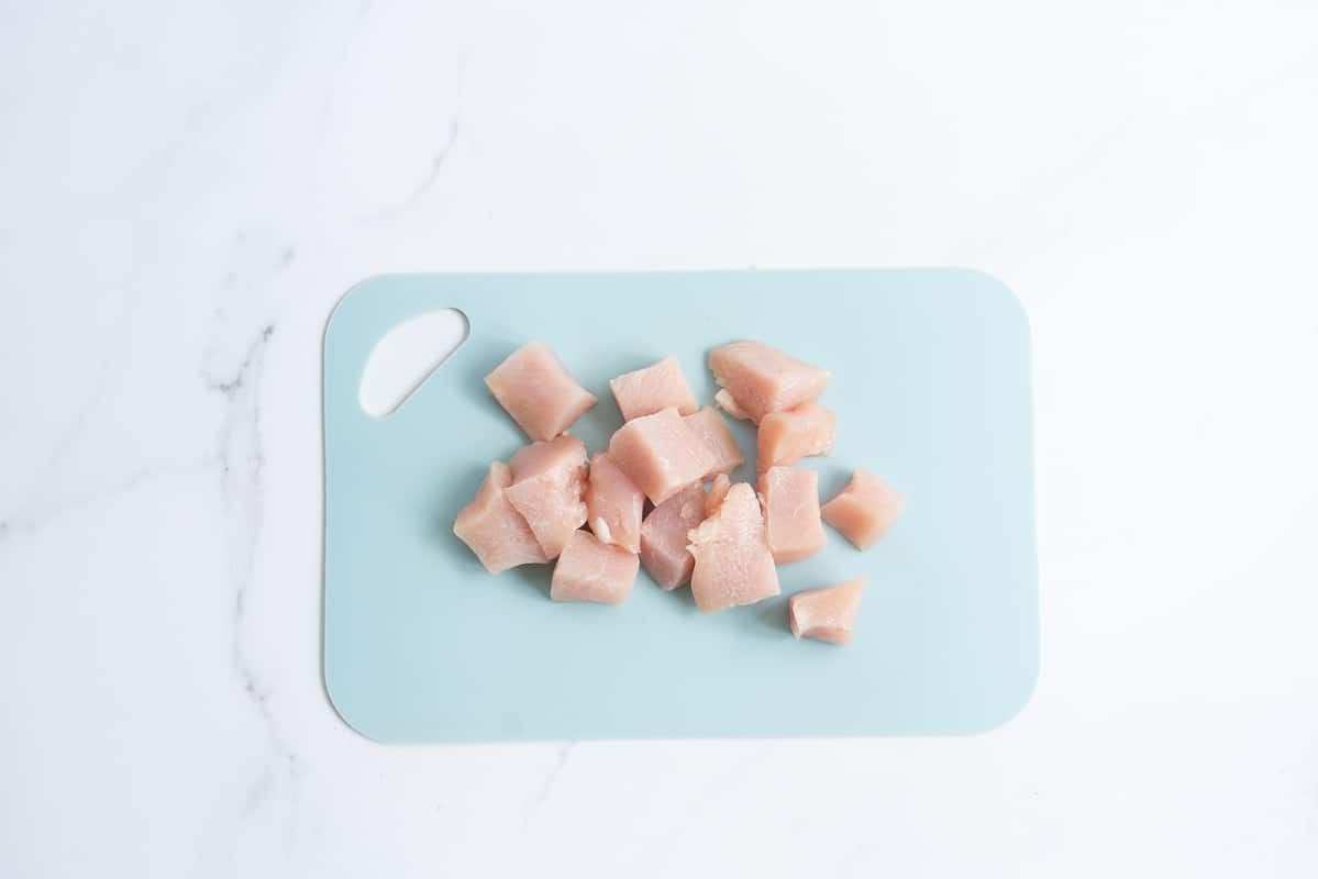 Chicken breast cut into bite sized pieces on a light blue chopping board.