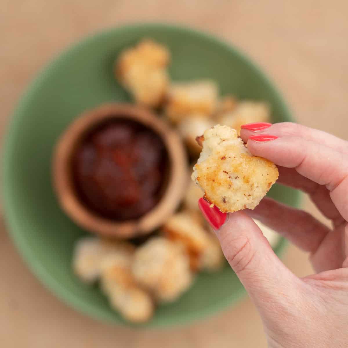 Women's hand holding a chicken nugget above a green platter of nuggets