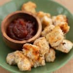 Crumbed chicken nuggets in a green bowl with a small bowl of tomato sauce.