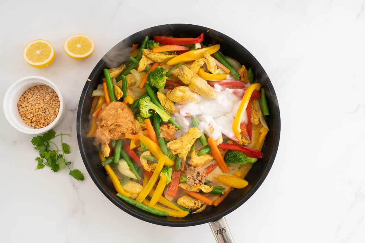 Stir fry vegetables and chicken with coconut cream and peanut butter visible in the pan.