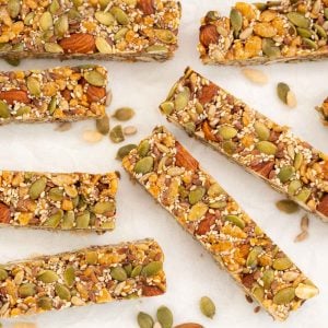 Energy bars on white crumpled baking paper surrounded by scattered nuts and seeds.