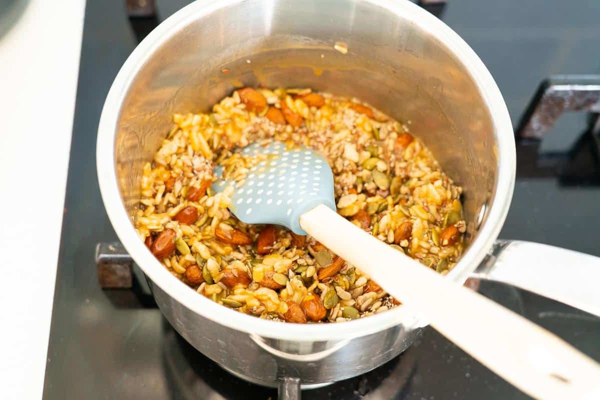 Nuts and seeds stirred through caramel in a saucepan.