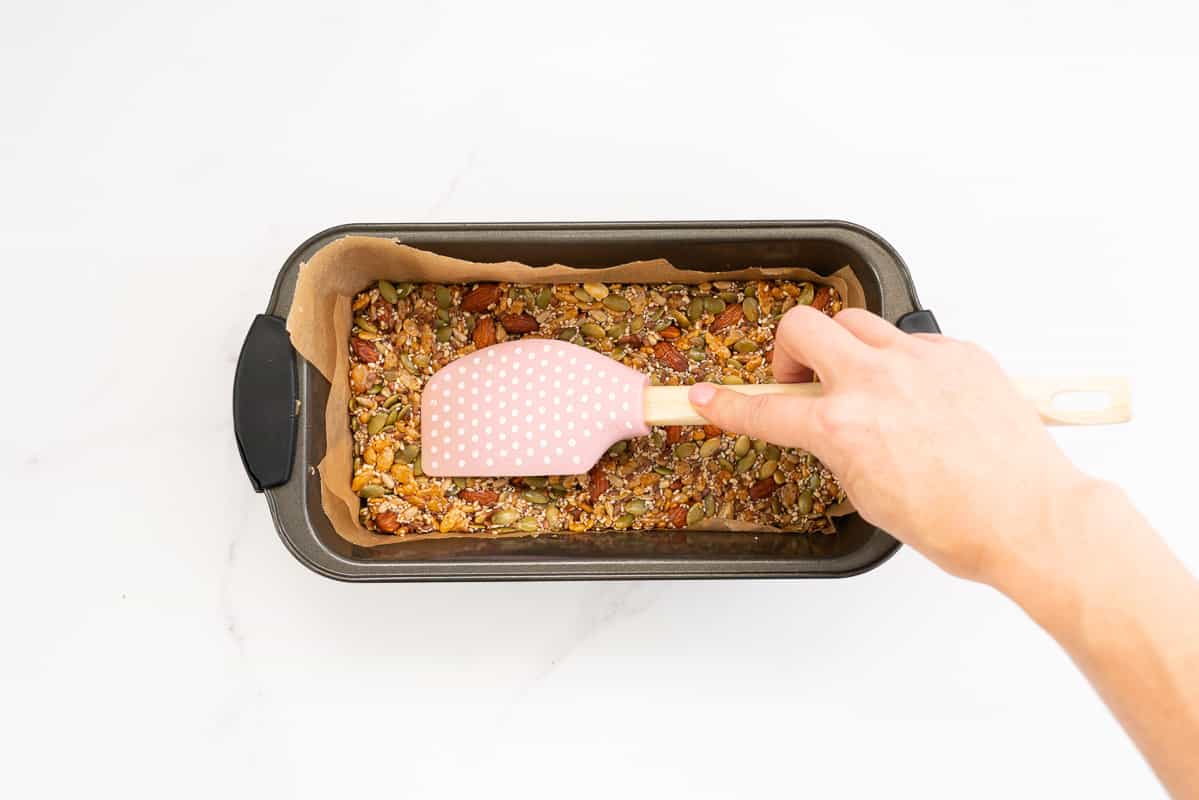 Energy bar mix being pressed into a loaf tin with a pink rubber spatula.