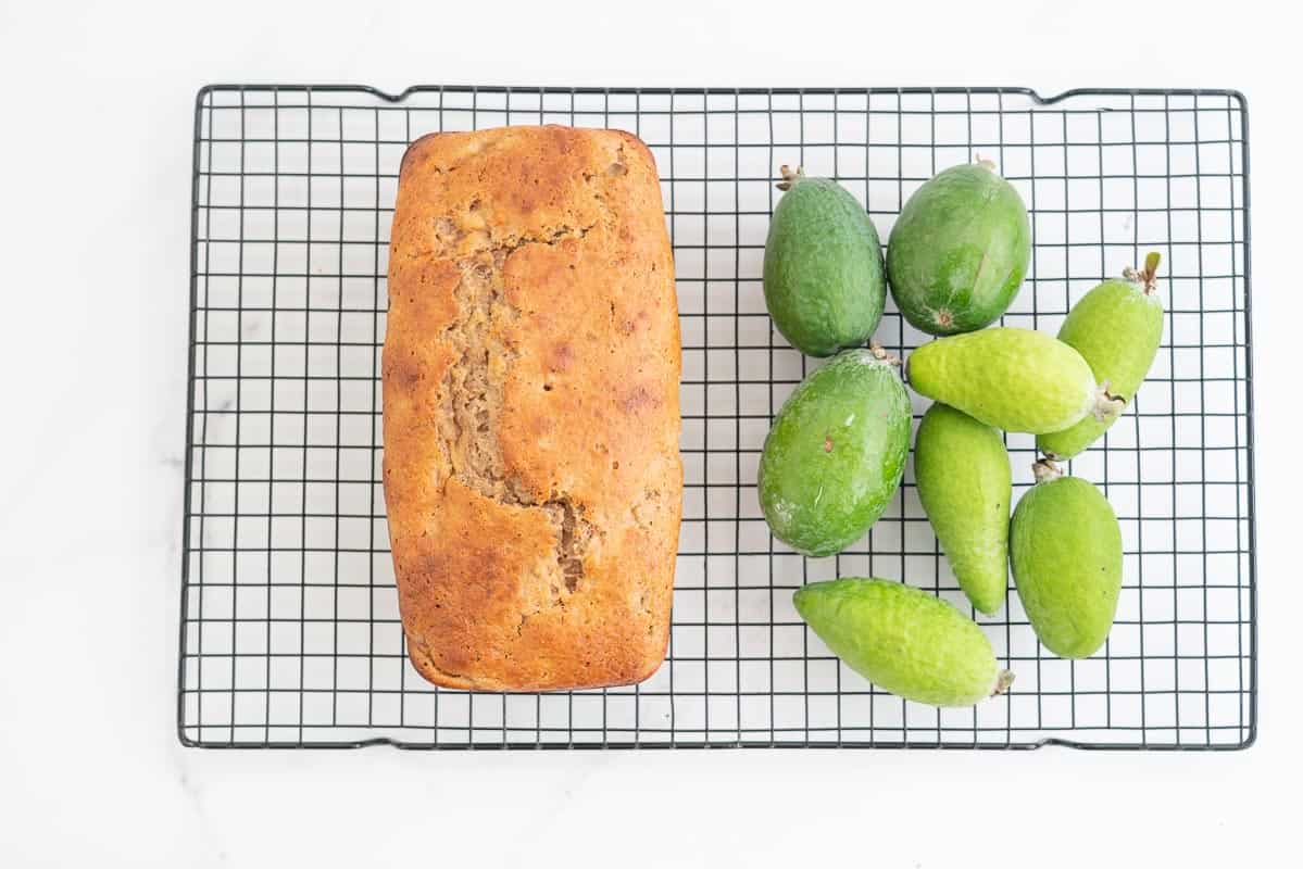 Golden brown loaf sitting on a cooling rack next to a pile of feijoas.