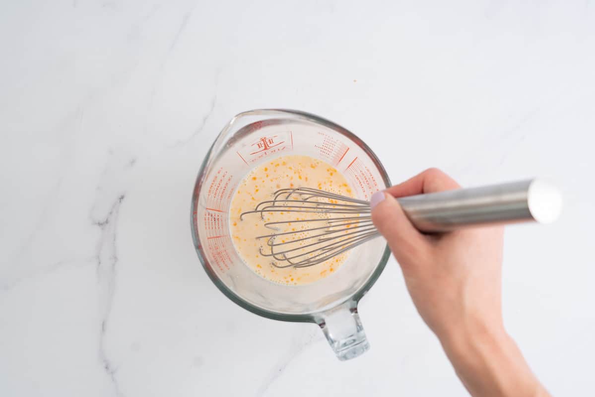 Egg, milk and vanilla in a glass jug being whisked together.