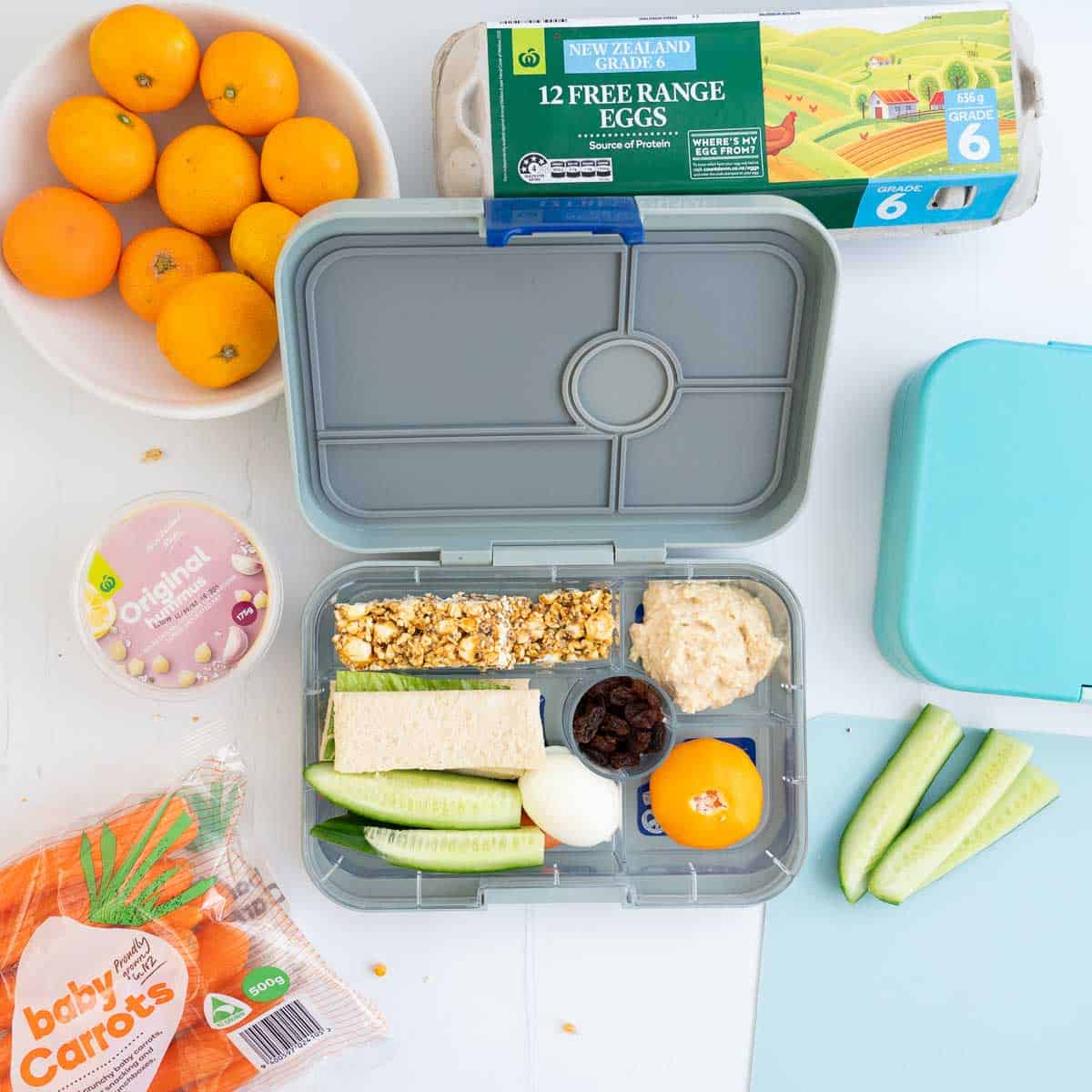 A child's bento style lunchbox packed with an assortment of food including popcorn bars.