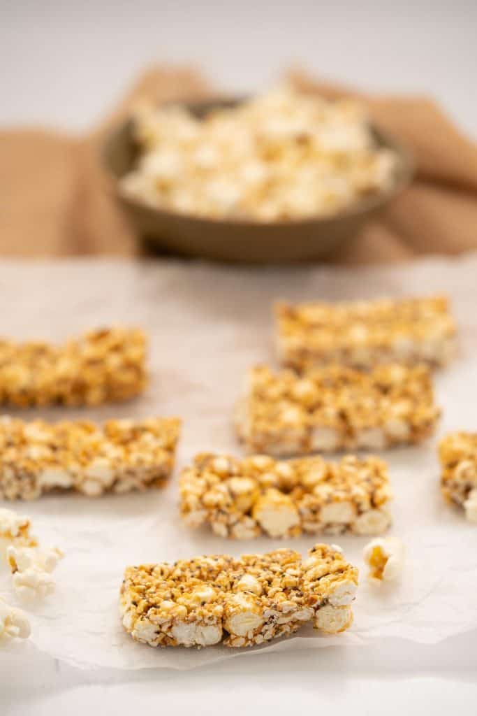 Popcorn bars sitting on a piece of baking paper, bowl of popcorn in the background.