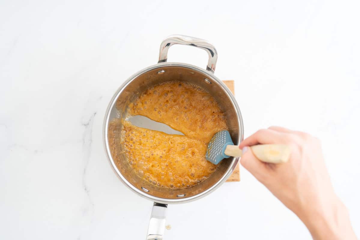Bubbling caramel in the bottom of a large saucepan, a spatula drawn through the caramel has left a channel.
