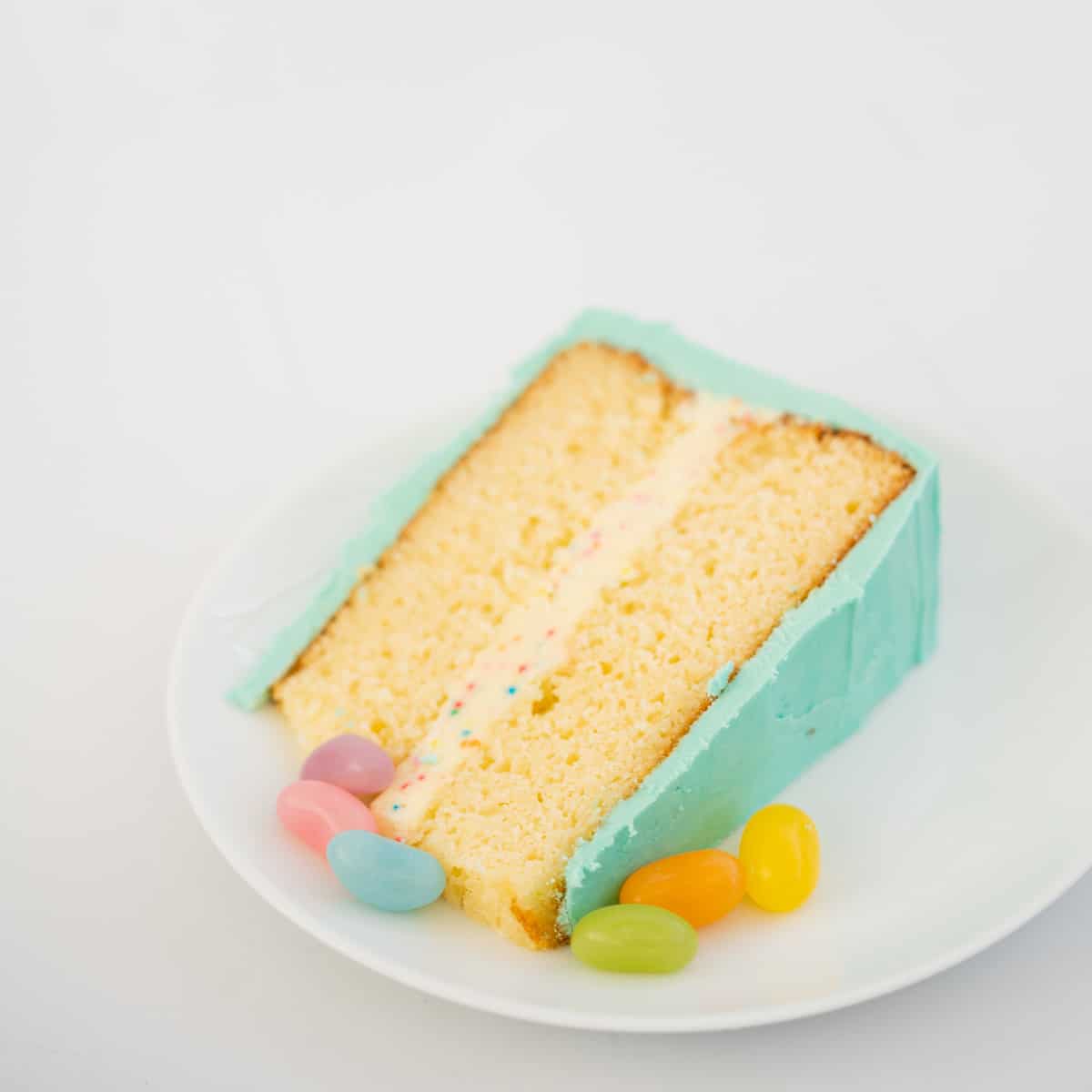 A slice of rainbow cake ready to serve on a white plate.