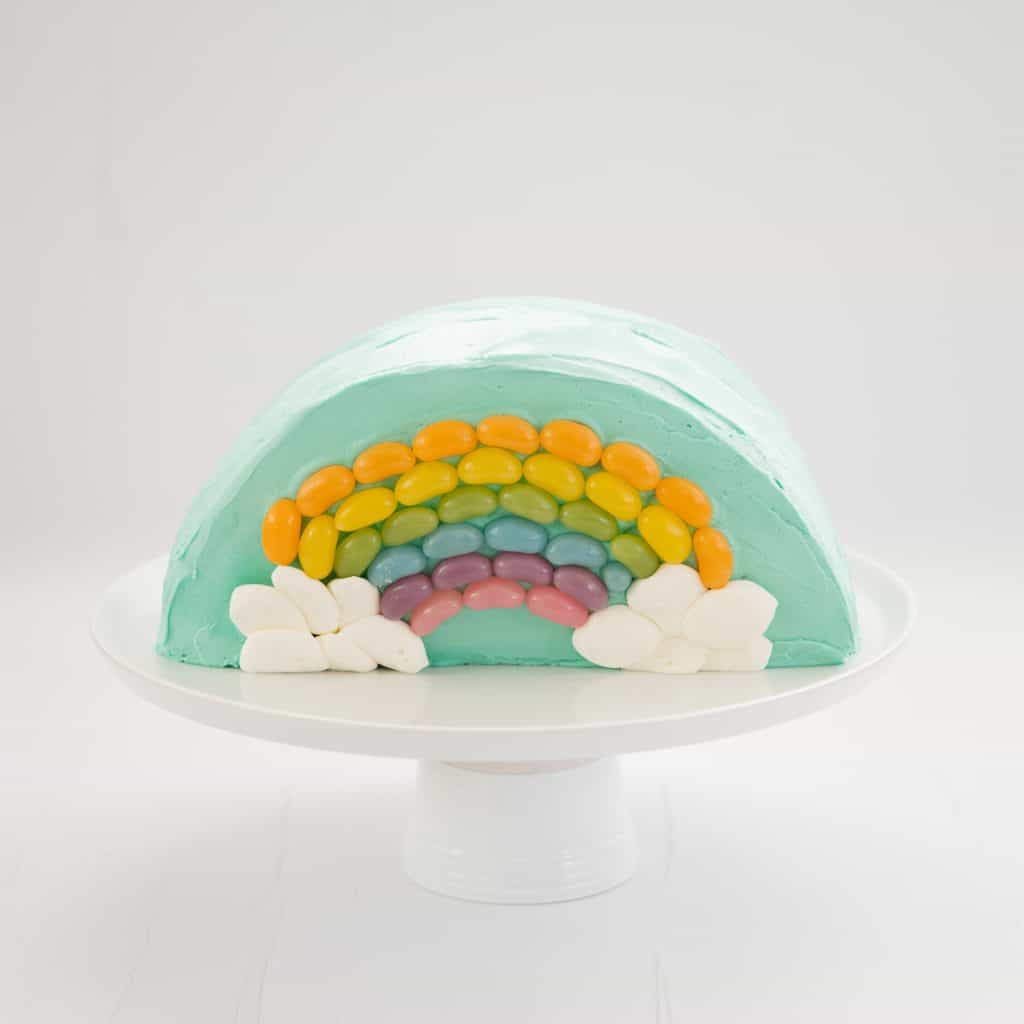 Rainbow Cake: Half round cake standing on a white serving platter decorated with a rainbow of jellybeans.
