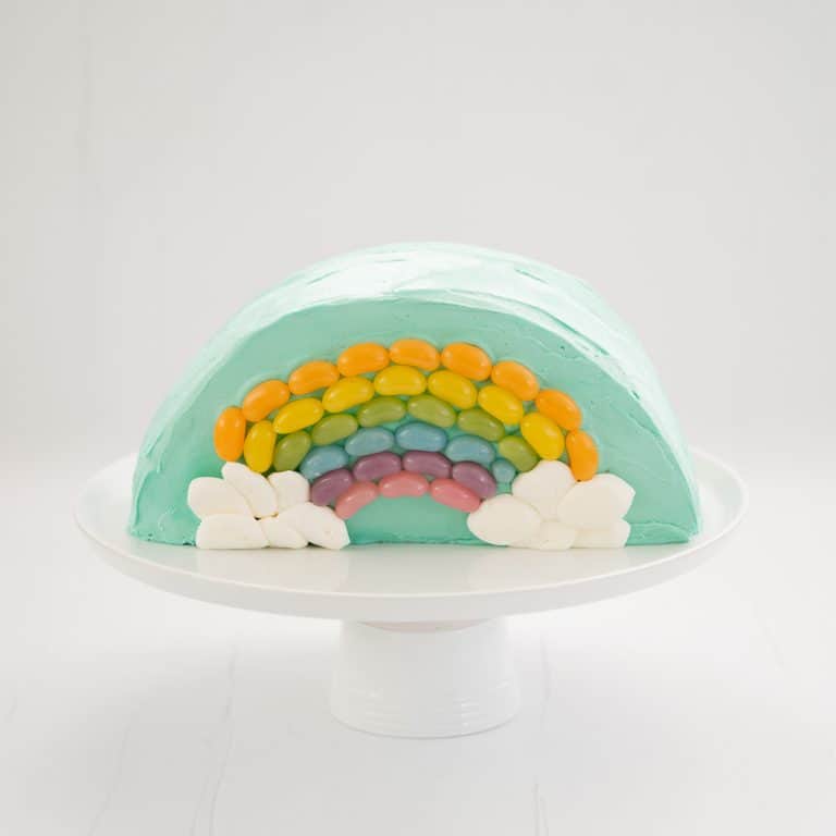 Rainbow Cake: Half round cake standing on a white serving platter decorated with a rainbow of jellybeans.
