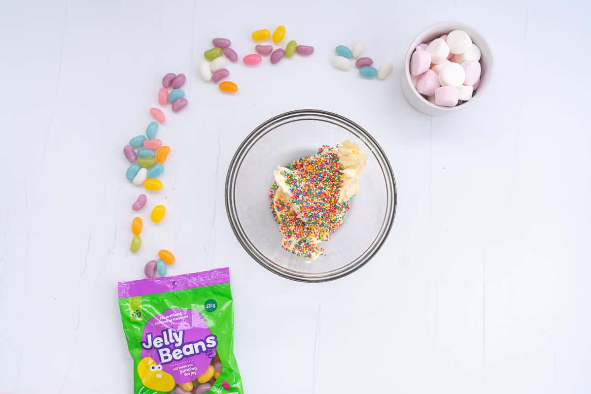 A glass bowl of buttercream with rainbow sprinkles added on top.