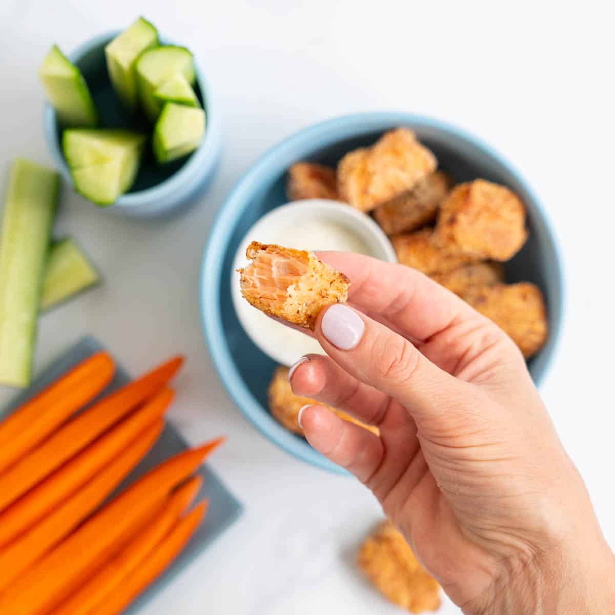 Women's had holding a crumbed piece of salmon.